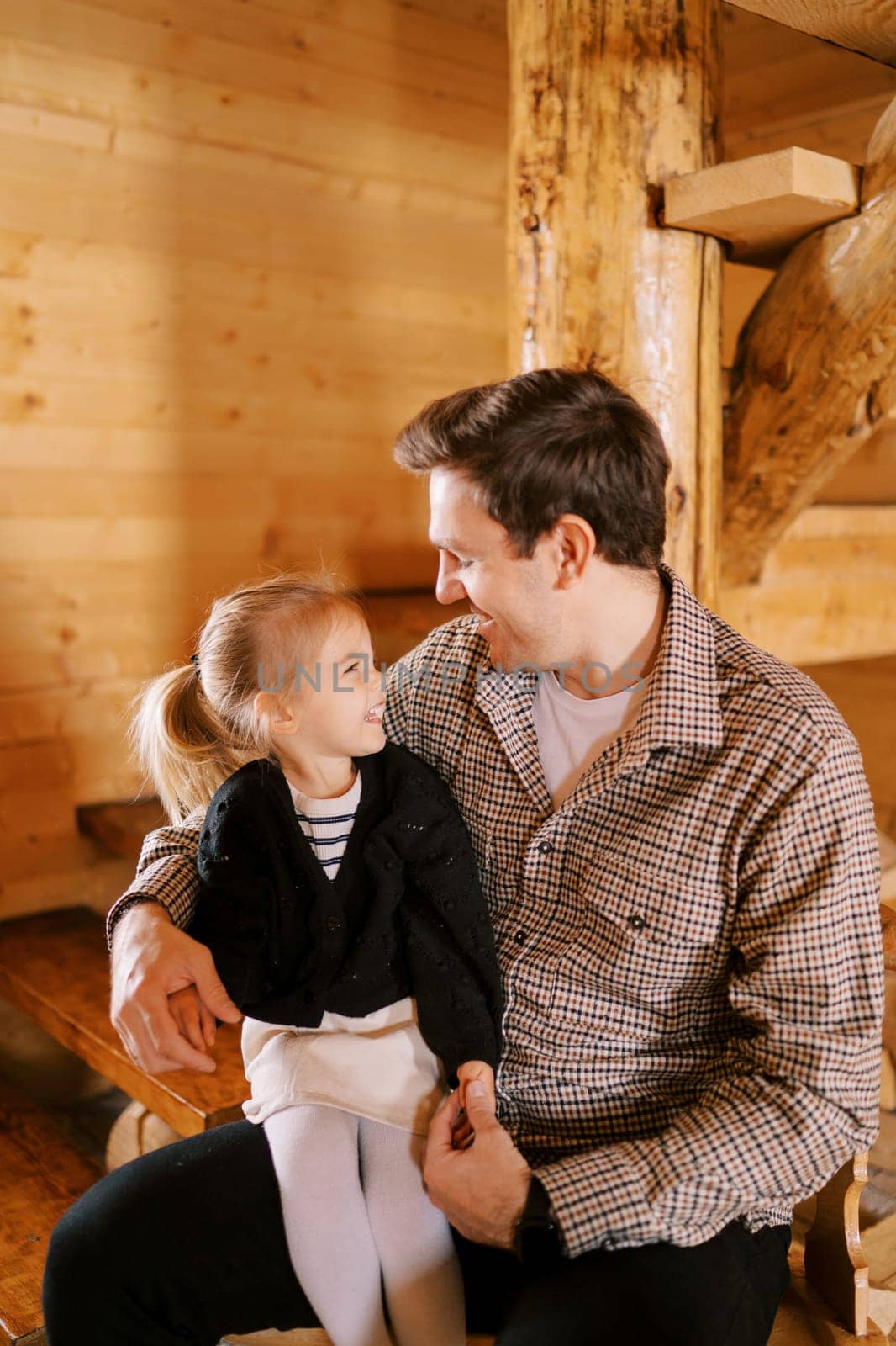 Smiling dad and little girl sitting on his lap looking at each other. High quality photo