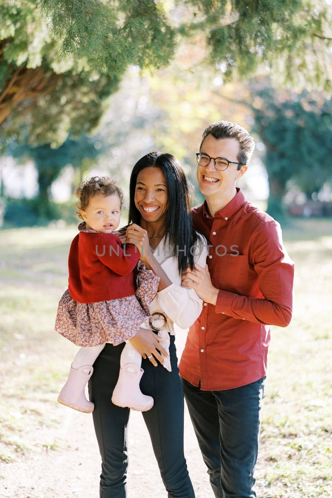 Smiling dad hugging laughing mom from behind with little girl in her arms. High quality photo