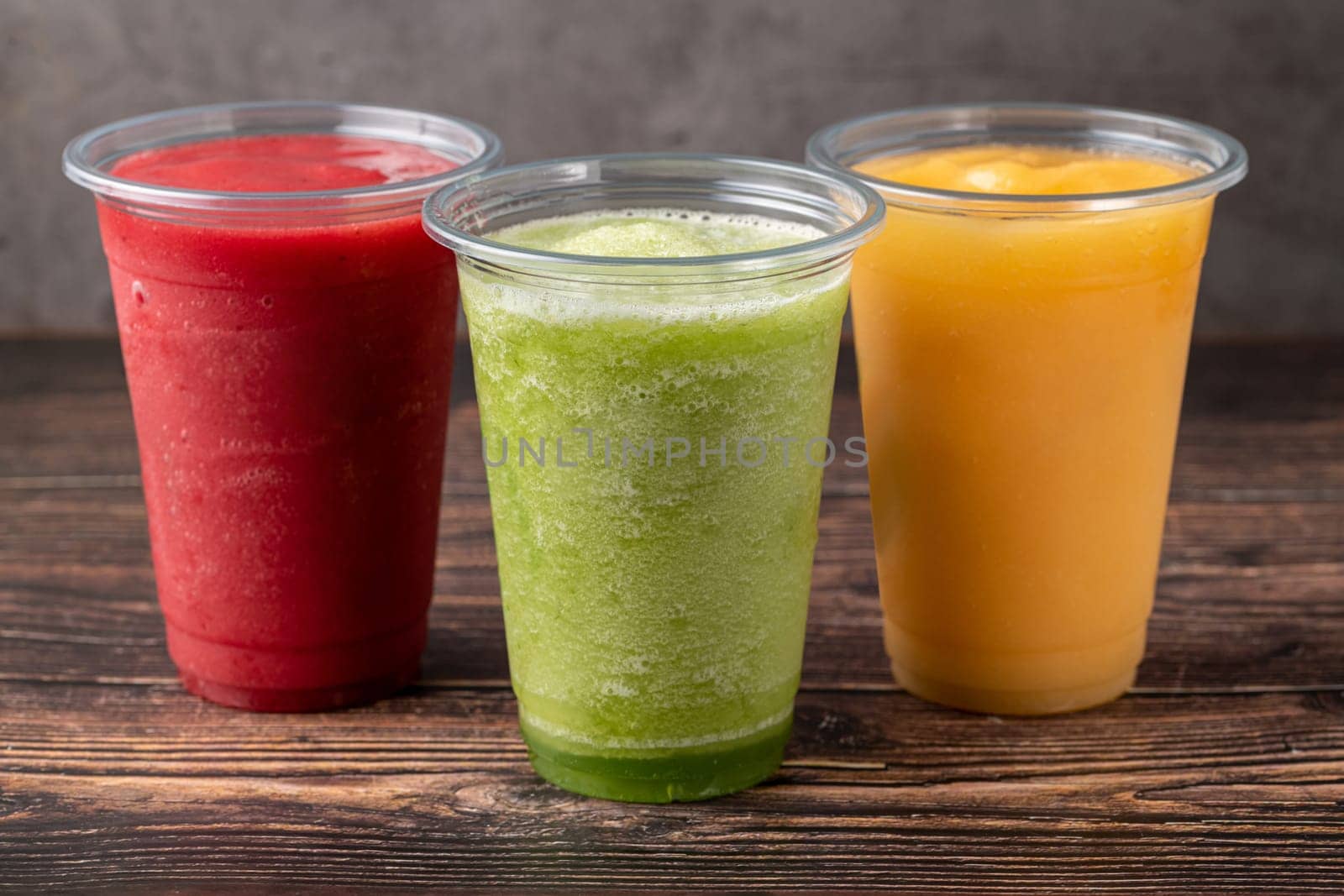 Three different fruit smoothies in plastic take away glasses on wooden background