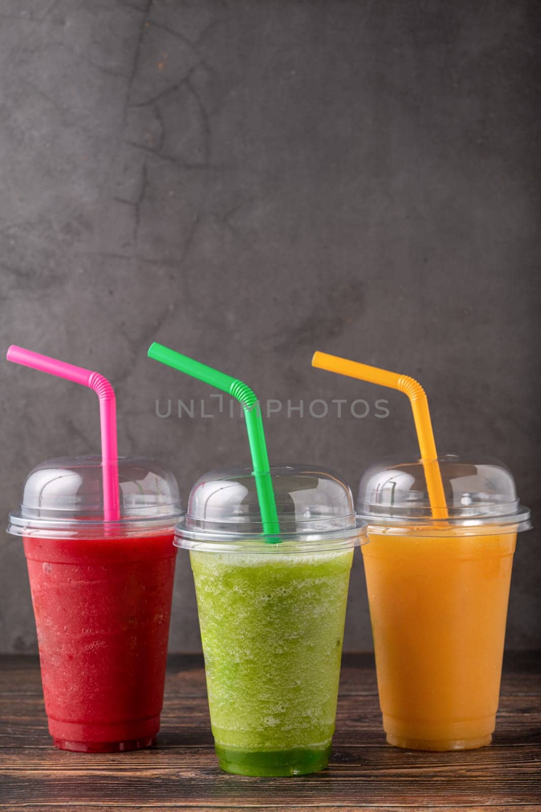 Three different fruit smoothies in plastic take away glasses on wooden background by Sonat