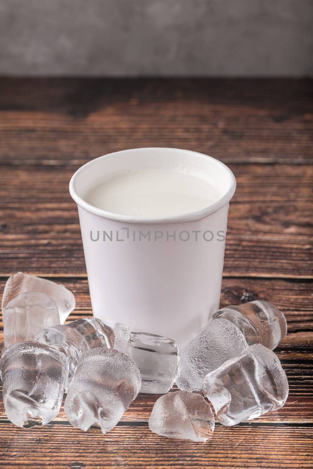 Cold milk in cardboard takeaway glass on wooden table