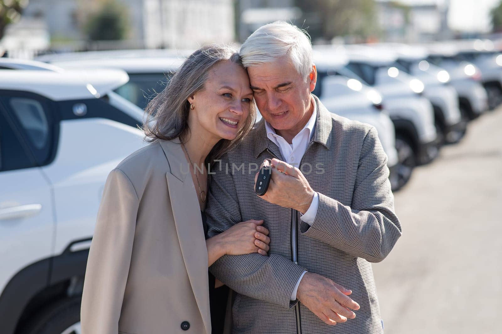 Mature Caucasian couple standing by a car outdoors. Elderly man holding car keys