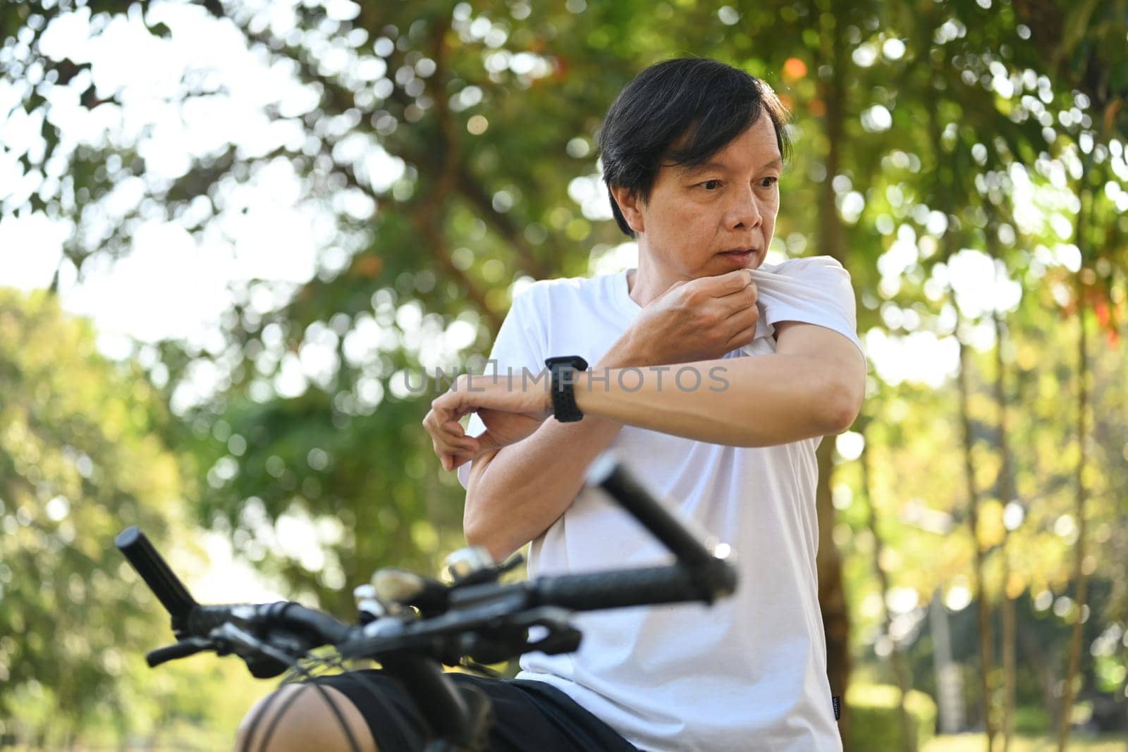 Tired middle age man taking a break from cycling in the park and wiping sweat on his face. by prathanchorruangsak