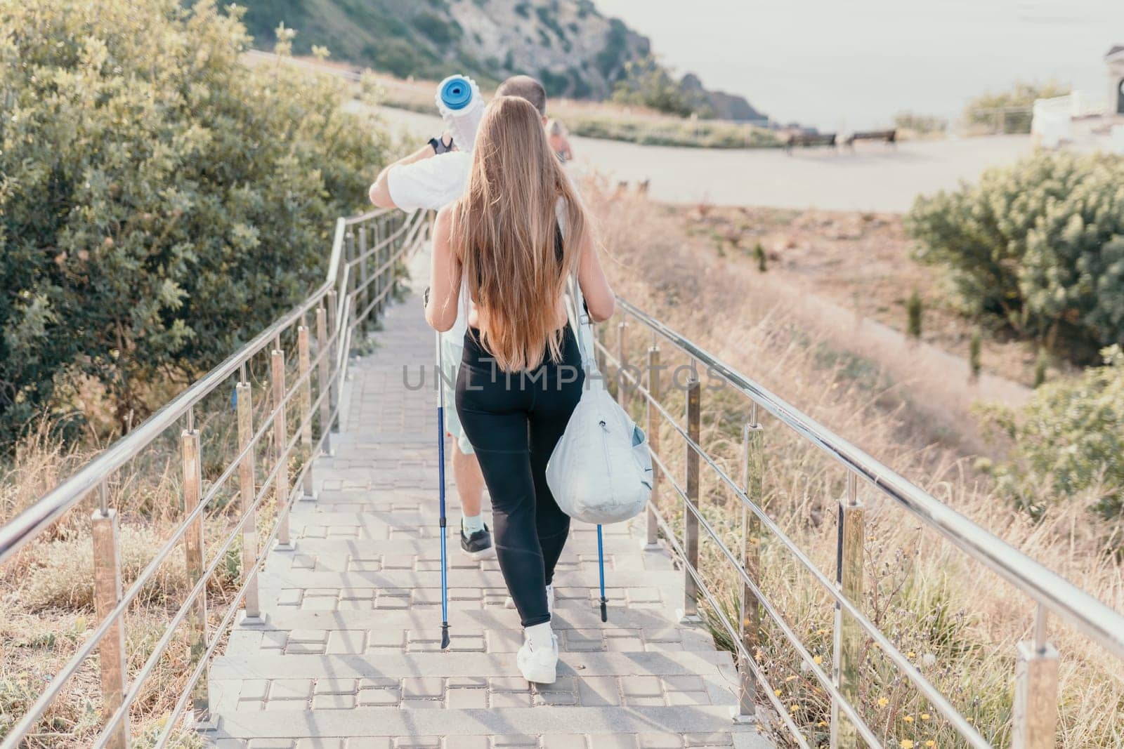 Happy Middle aged couple or friends practicing nordic walking in park near sea. Mature couple with trekking poles walking, practicing Nordic walking outdoors. Aging youthfully and sport concept.