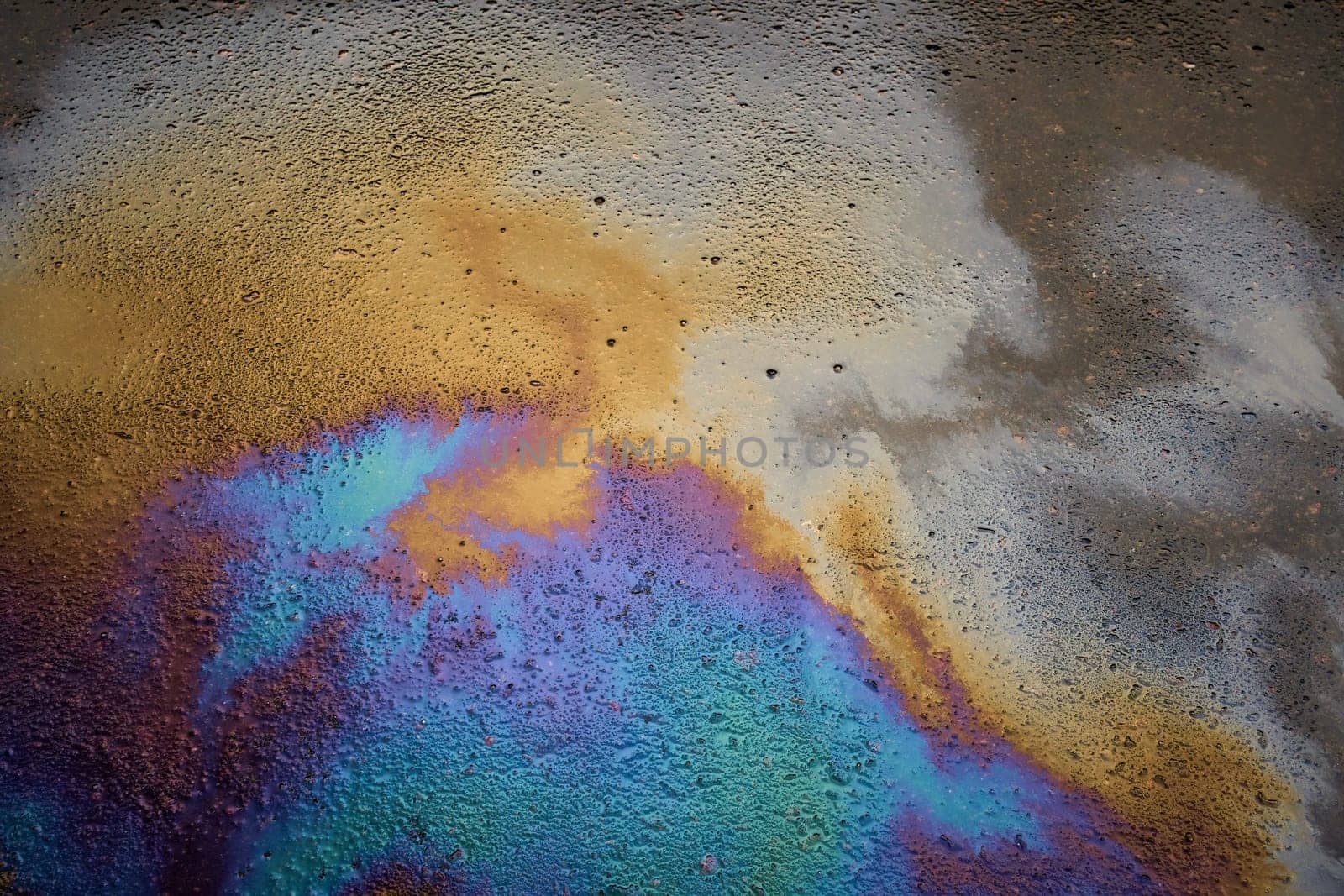 Multi-colored poisonous spots of spilled gasoline on wet pavement during rain. Rain blurred the car oil from a malfunctioning car in a parking lot