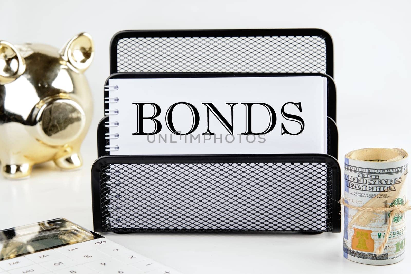 BONDS text on a white piece of paper next to a piggy bank, a roll of money and a calculator on a white background