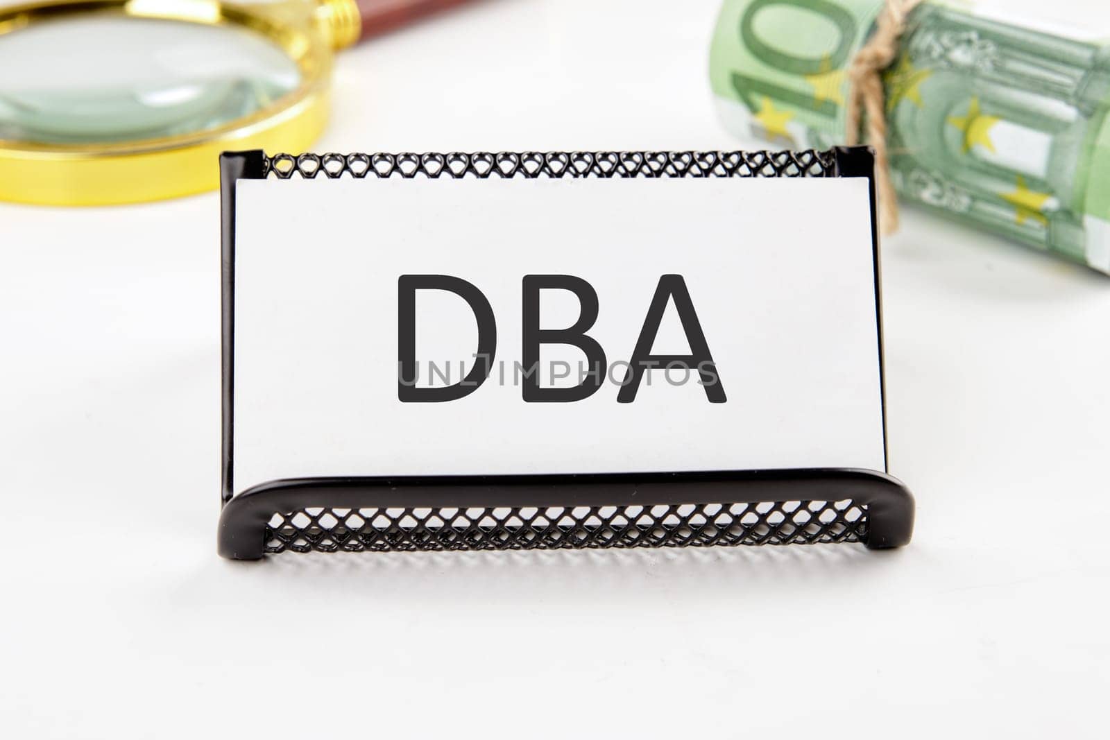 DBA the text on the business card next to the roll of money with a magnifying glass in the background is out of focus on a white background