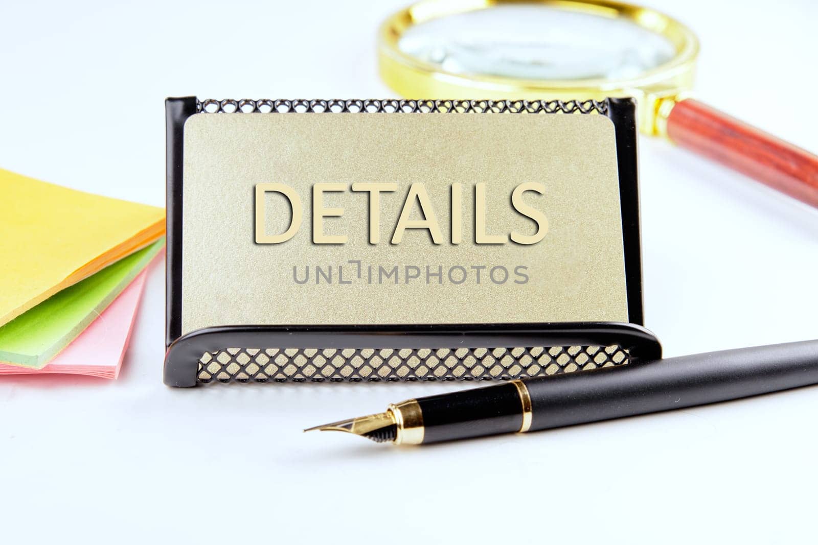 DETAILS text on a gold plastic card with convex text next to office supplies on a white background