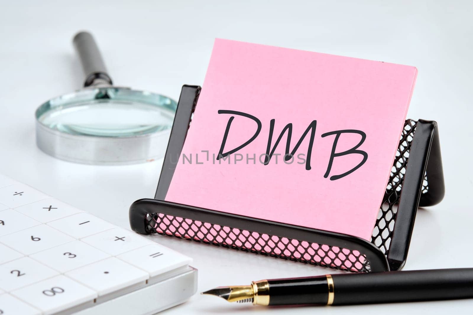 DMB word on the sticker on the stand on a white background next to a fountain pen, calculator and magnifying glass on a white background