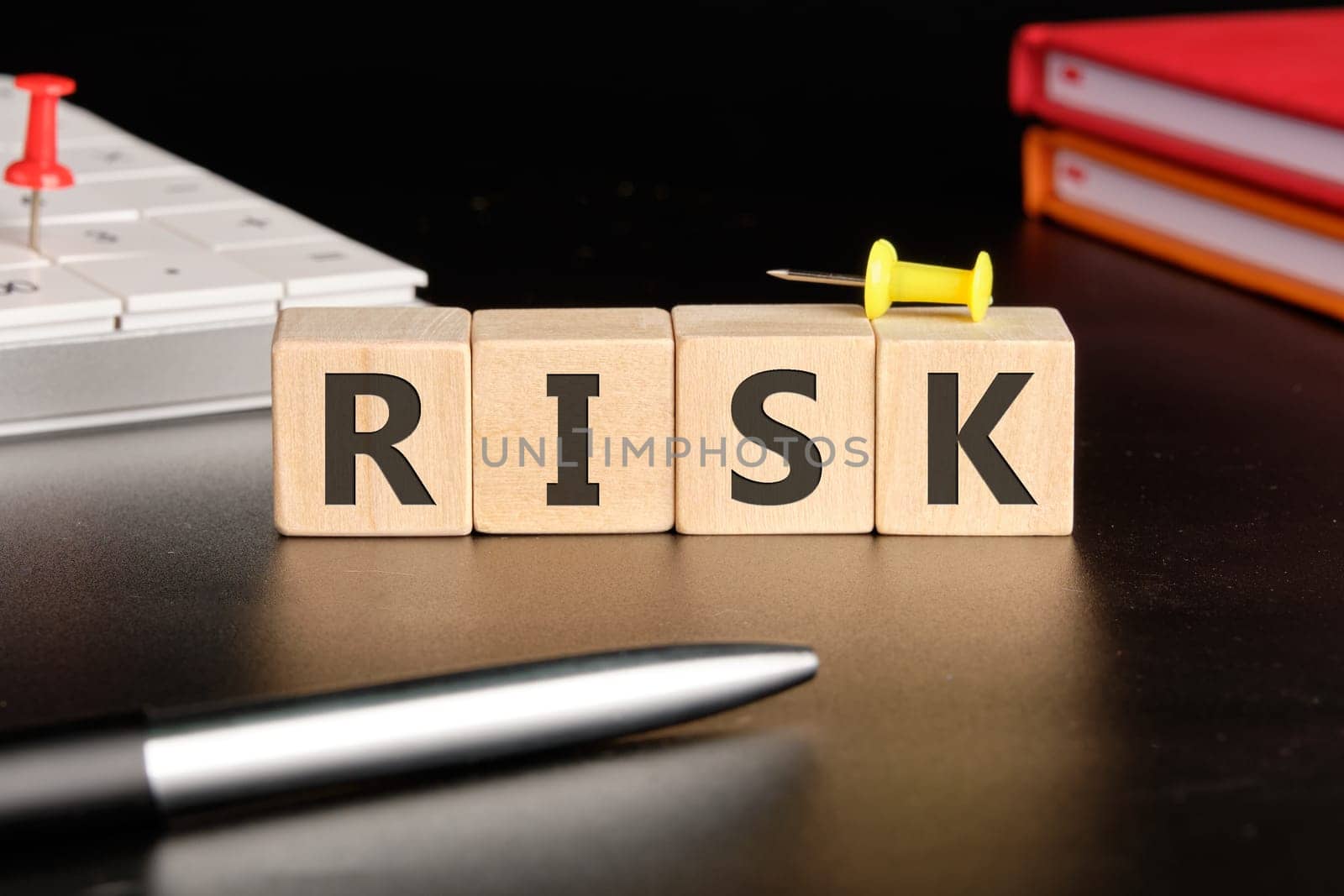 RISK the text of non-wooden cubes next to notepads, a calculator, a pen on a black background