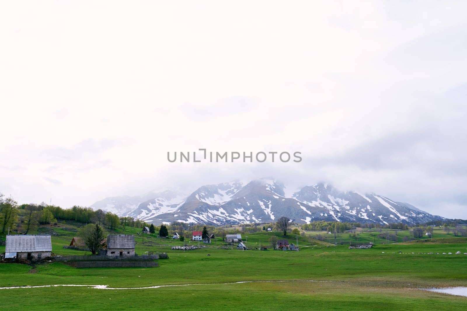 Village in a green valley at the foot of foggy snowy mountains. High quality photo