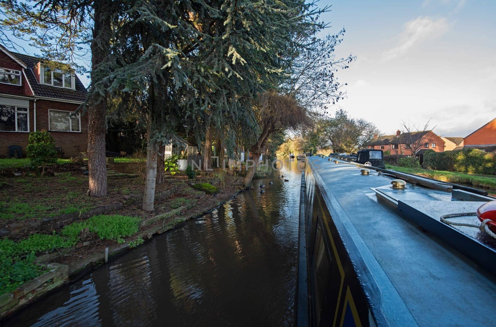 View from a narrowboat travelling in English urban countryside scenery on British waterway canal through village