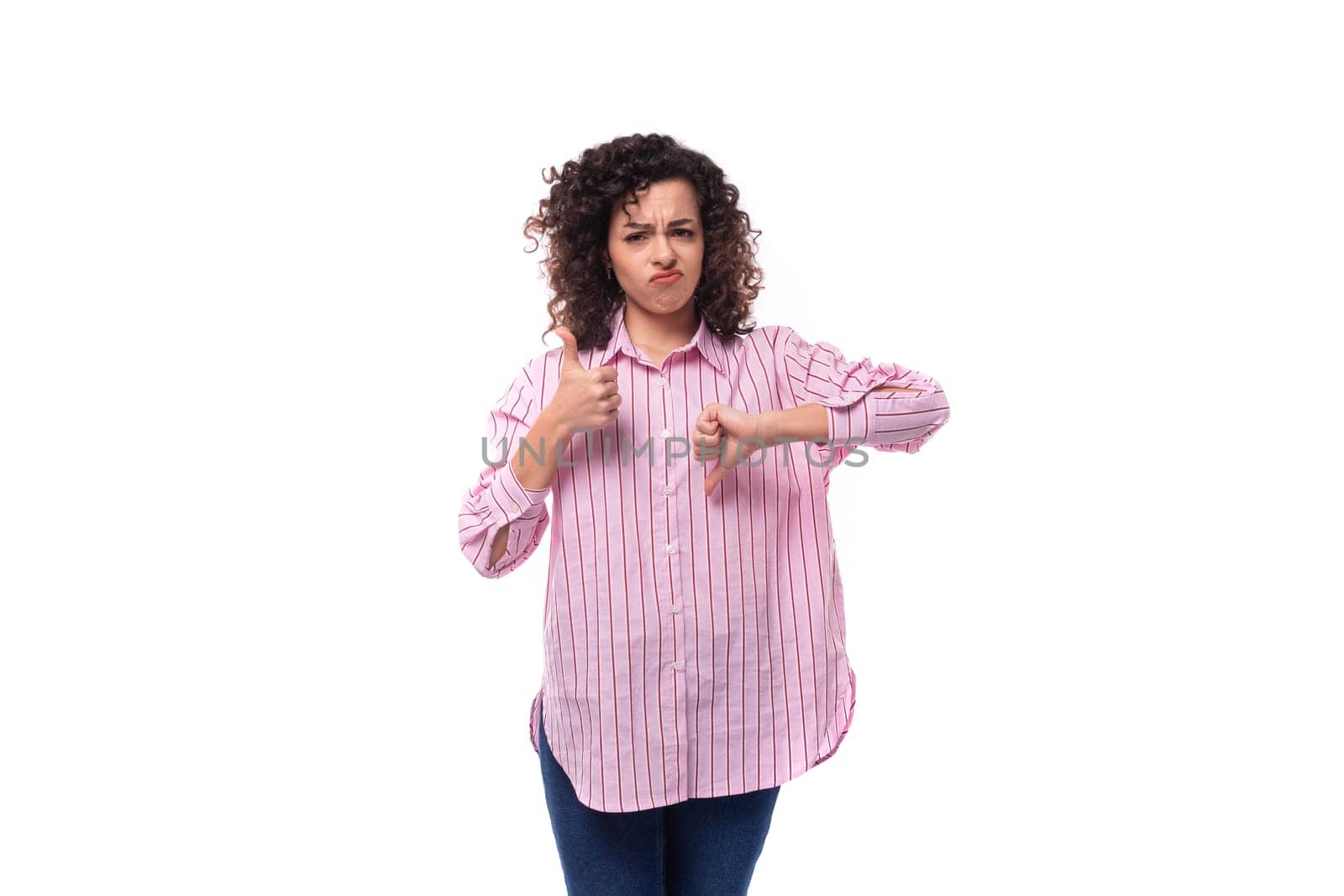 young curly brunette model woman dressed in a pink striped shirt shows like and dislike.
