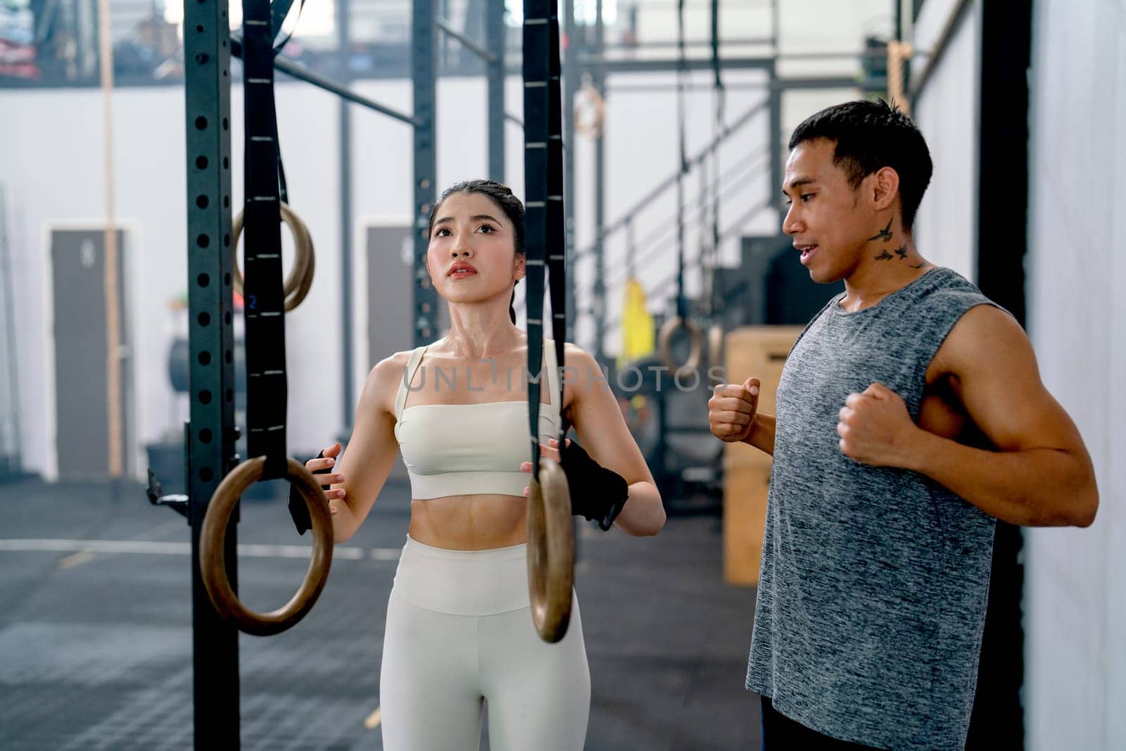 Asian coach or trainer man help and support sport woman to exercise with loop in fitness gym and also show example of good position of training.