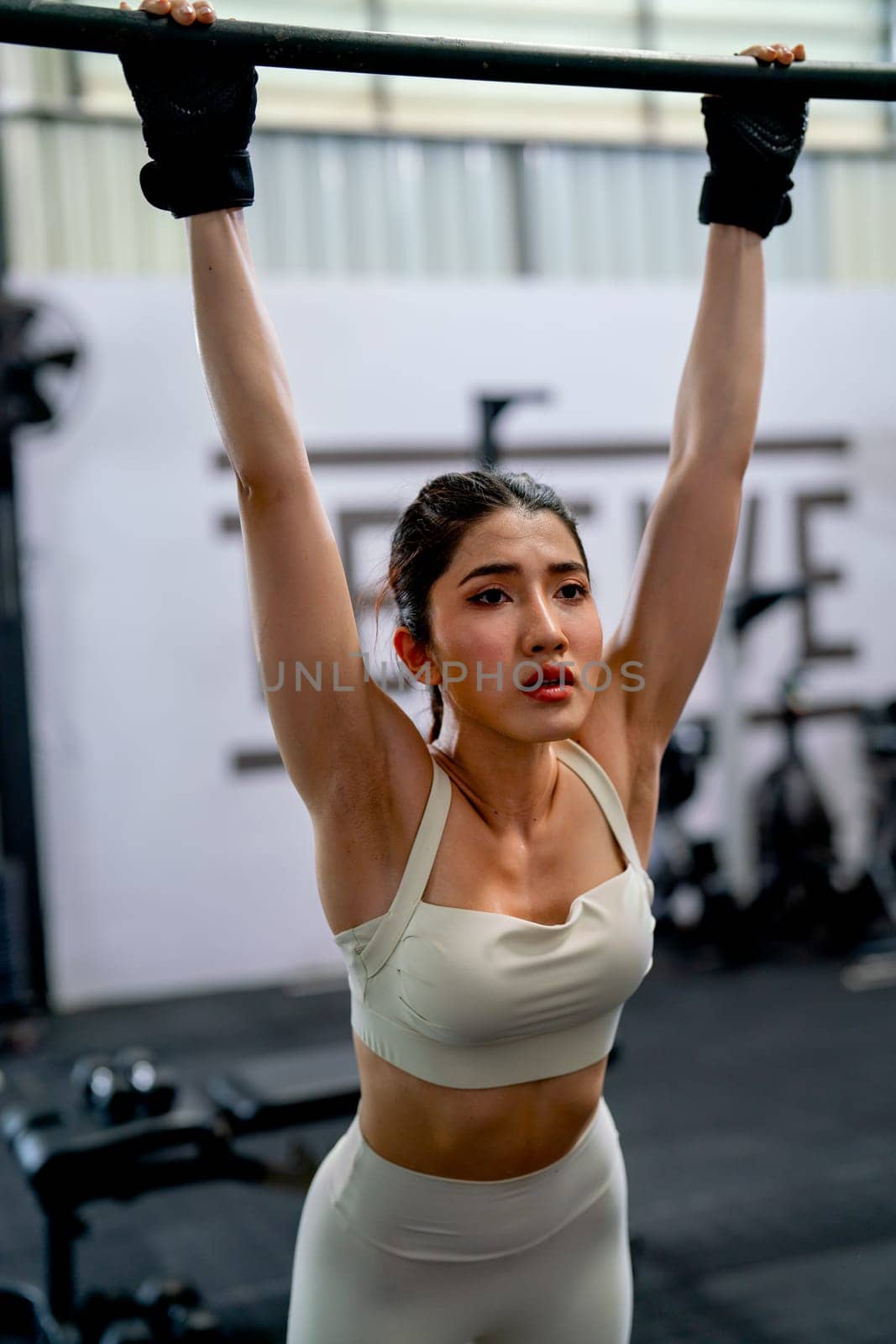 Asian sport woman stand and hanging bar look like relax after exercise in fitness gym with happiness.