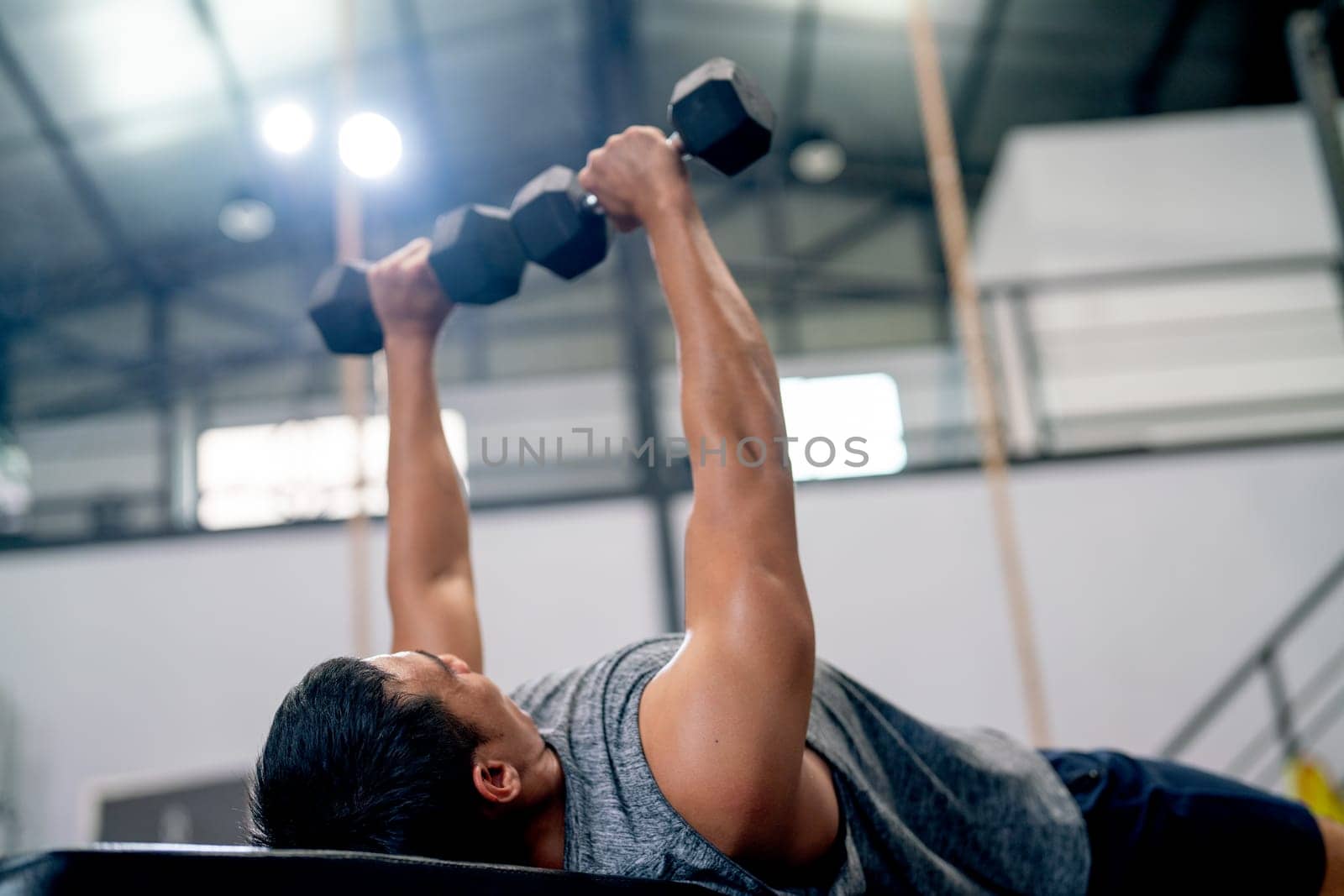 Close up sport man lift dumbells up to over head during lie on long chair in fitness gym.