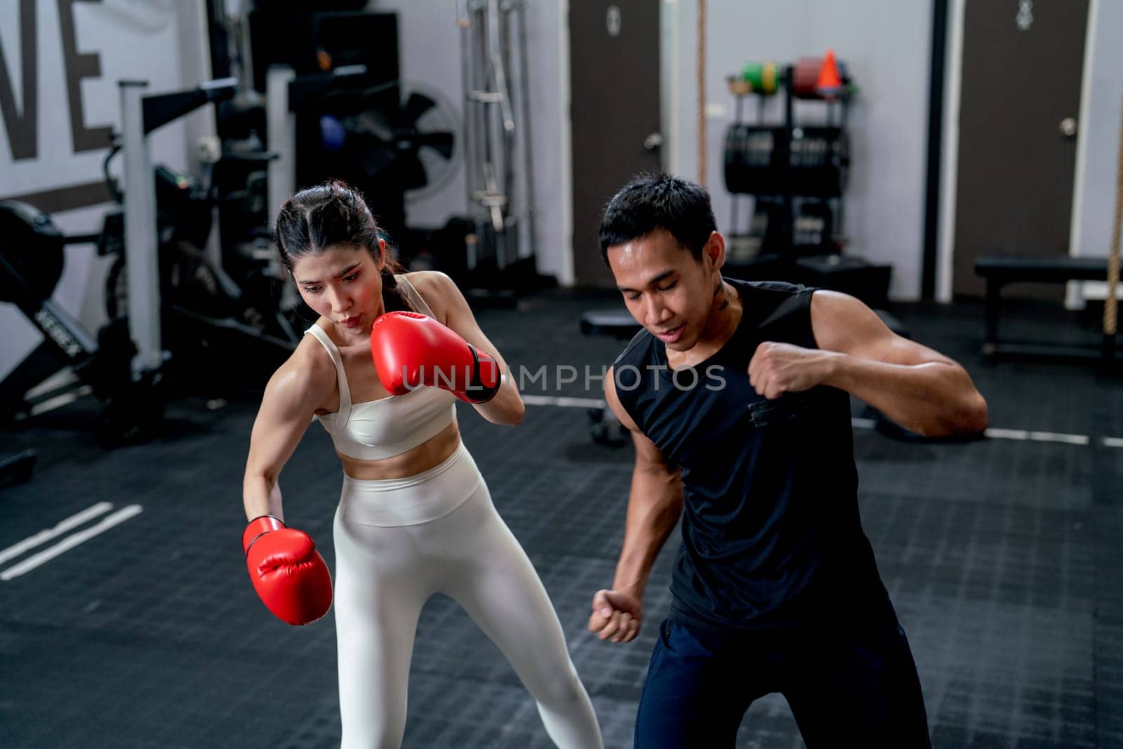 Asian sport trainer man help woman to practice with boxing for good action and movement in fitness gym.