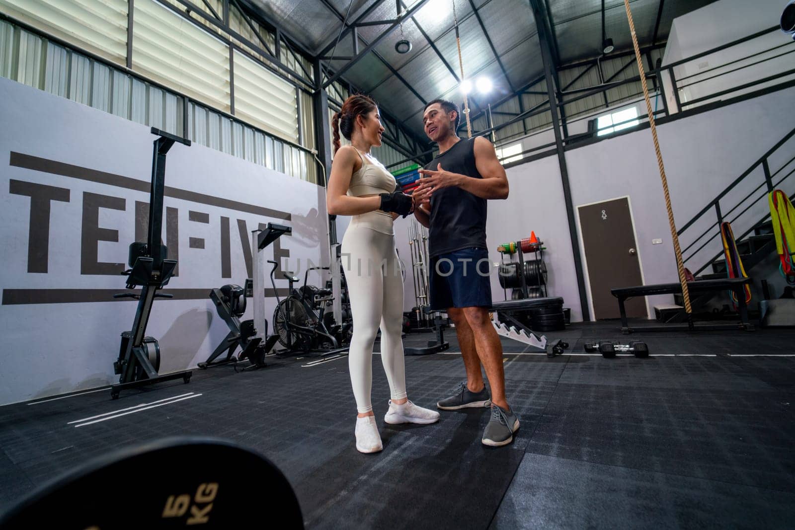 Wide shot of Asian sport man and woman stand and discuss together in fitness gym with happiness.