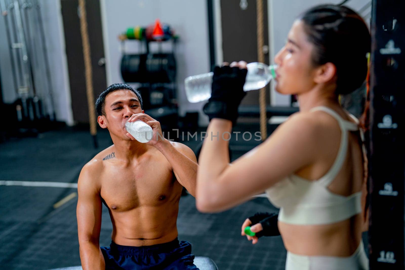 Asian sport man and woman drink water from bottle after finish of training in fitness gymm.