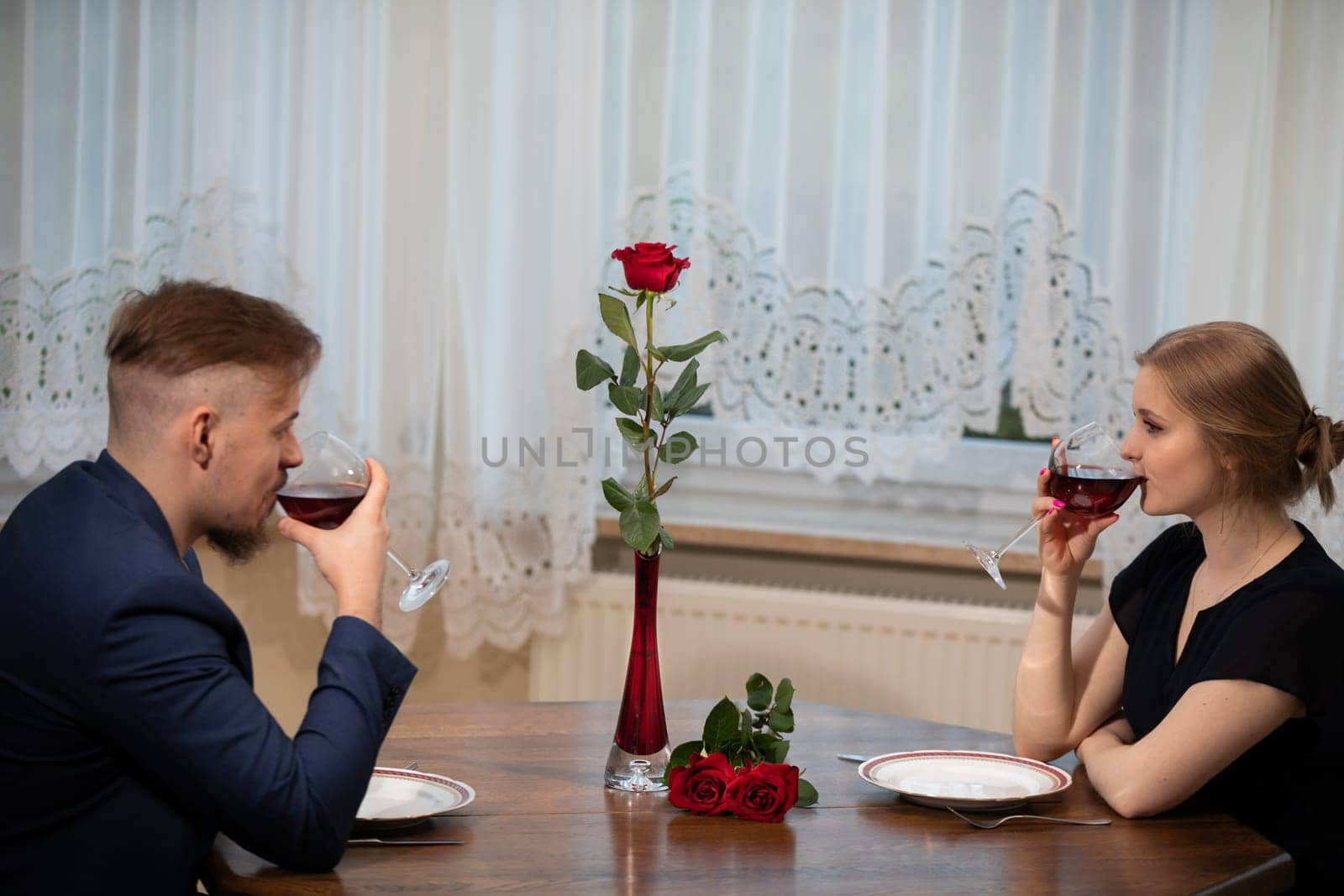 A man and a woman drink red wine from glasses. They are sitting at the table. There are empty plates in front of them. Celebrating an important occasion in formal clothes.