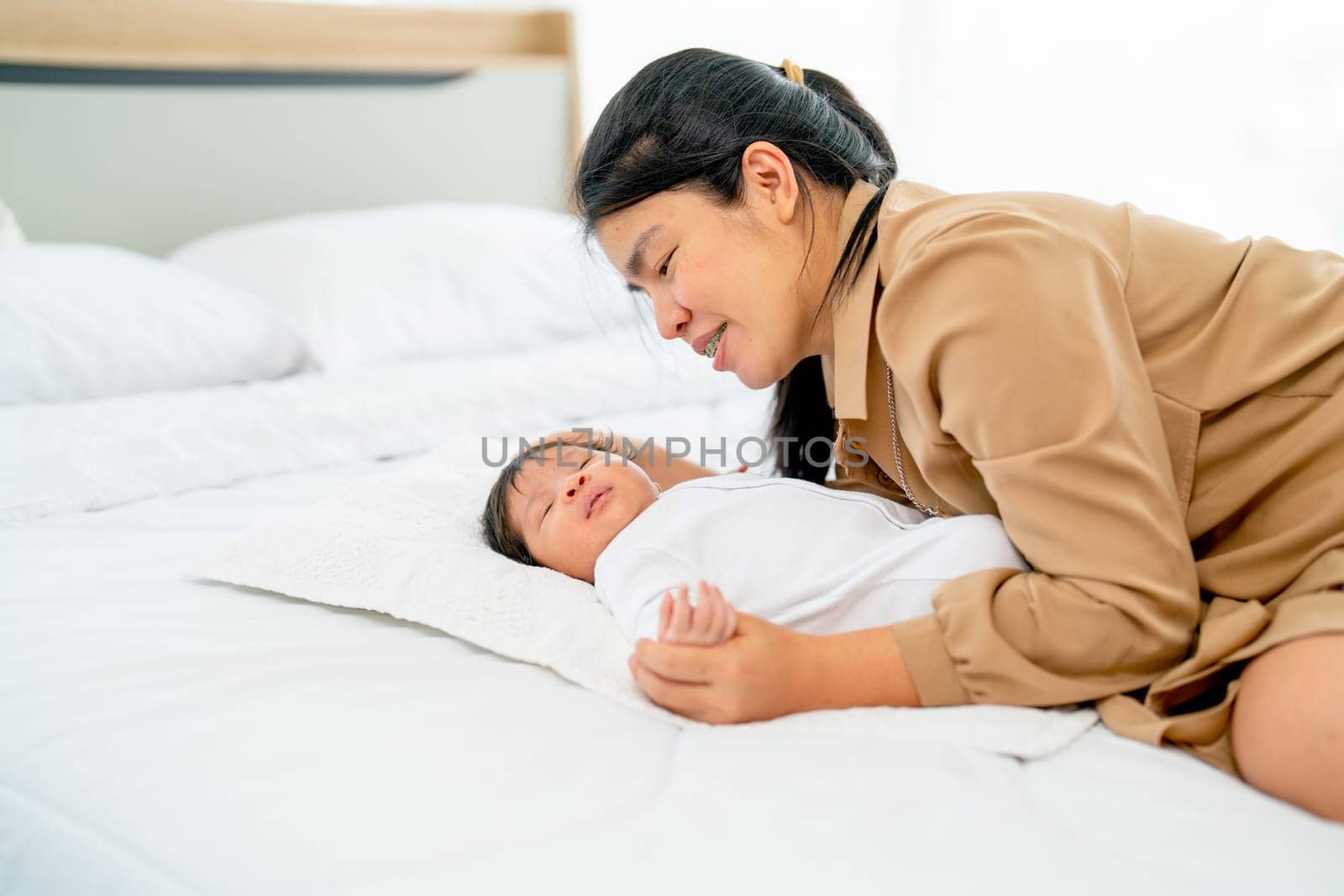 Asian mother lie beside of newborn baby sleep on bed in bedroom with day light and they look relax and happiness.
