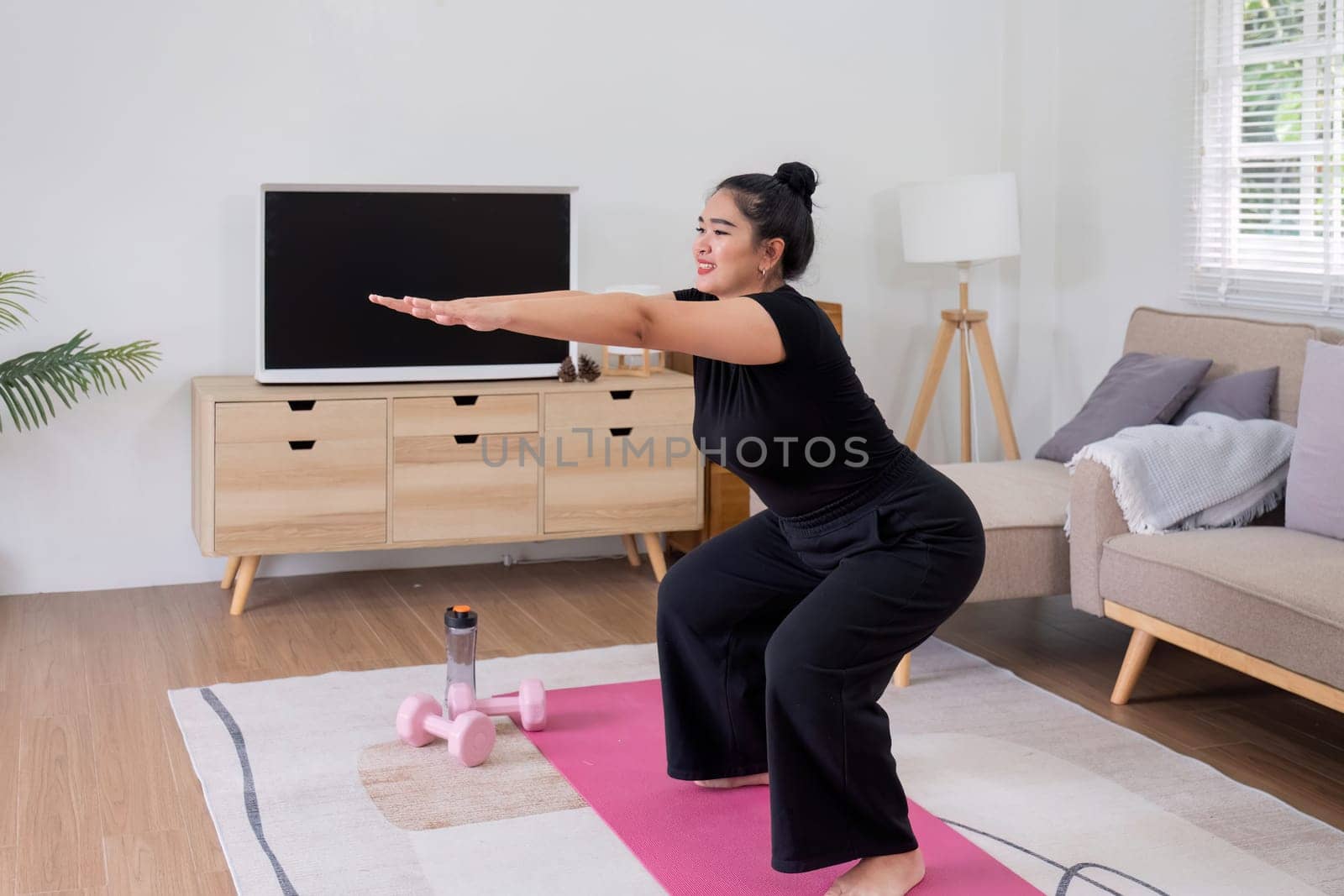 Fat woman exercising at home A beautiful oversized woman in a sports bra and casual pants stands in the living room and exercises..