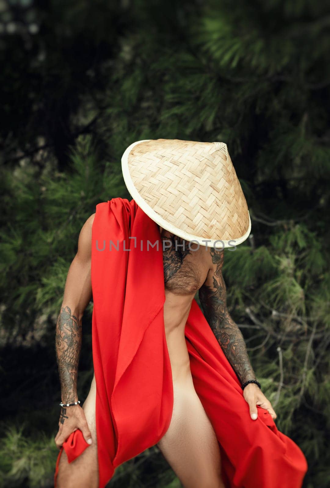 Sexy male monk in red cape and an Asian triangular hat with tattoos in nature by Rotozey