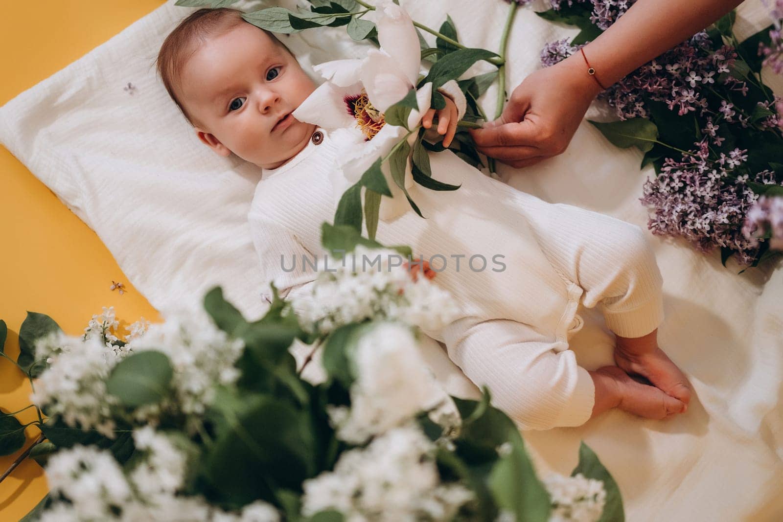 A cute baby is lying on a blanket among flowers. Spring concept. High quality photo