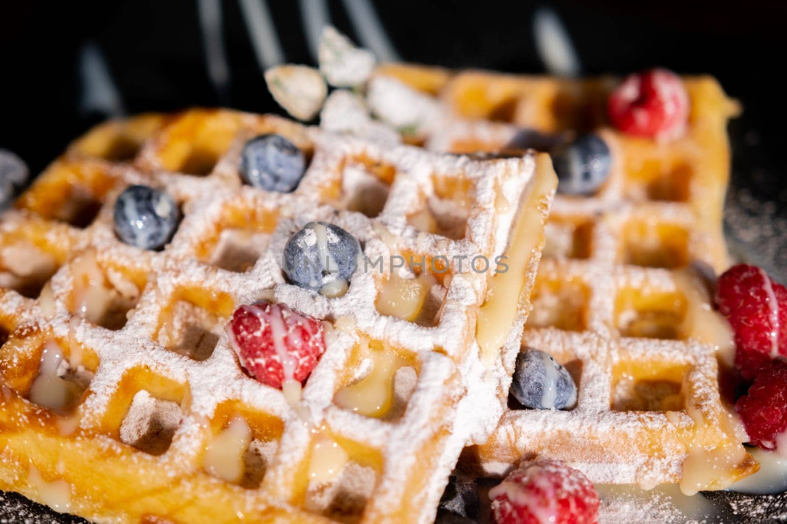 Belgian French waffles close-up with berries, blueberries athens raspberries blueberries sprinkled with powdered sugar, condensed milk, side view isolated on black background. Sweet breakfast dessert