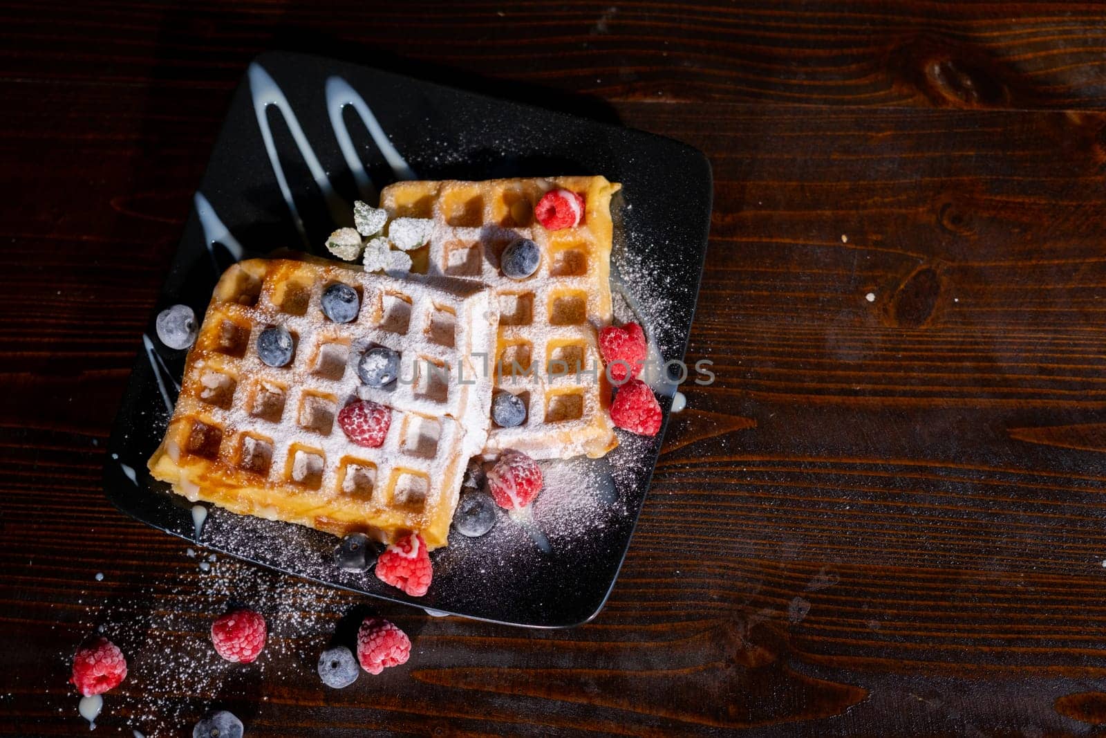 Belgian French waffles close-up with berries, blueberries athens raspberries blueberries sprinkled with powdered sugar, condensed milk, side view isolated on black background. Sweet breakfast dessert