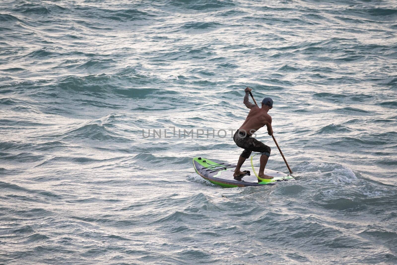 athletic wiry surfer guy swims with a paddle on a sup board in the sea Stand up paddleboarding