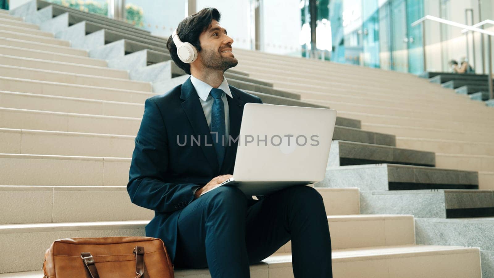 Professional business man sitting at stairs while working on laptop. Exultant. by biancoblue