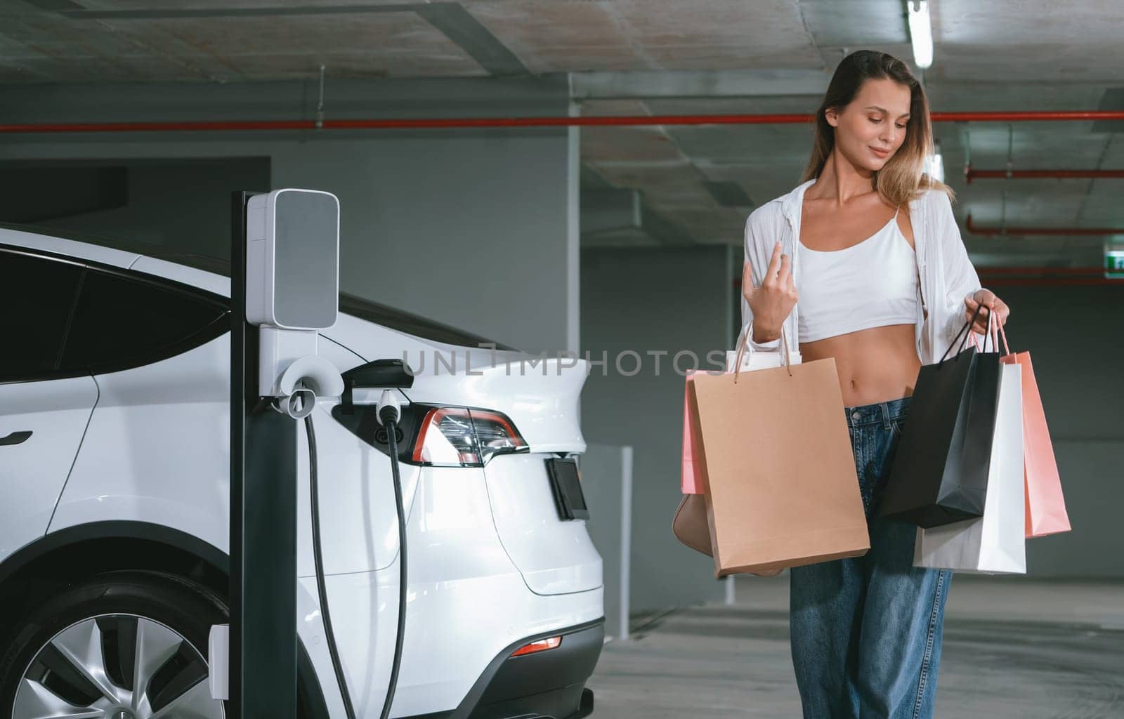 Young woman travel with EV electric car to shopping center parking lot charging in downtown city showing urban sustainability lifestyle by green clean rechargeable energy of electric vehicle innards