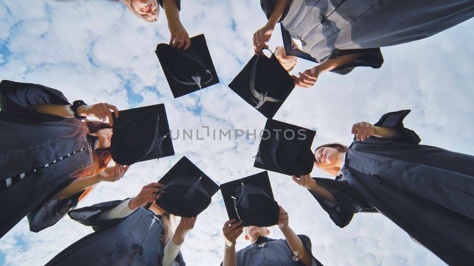 Graduates in black robes join their caps in a circle. by DovidPro