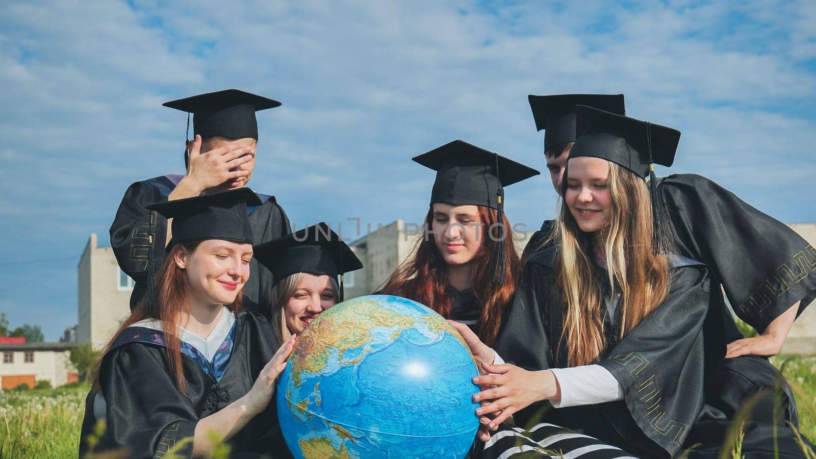 Graduates in black robes examine a geographical globe sitting on the grass