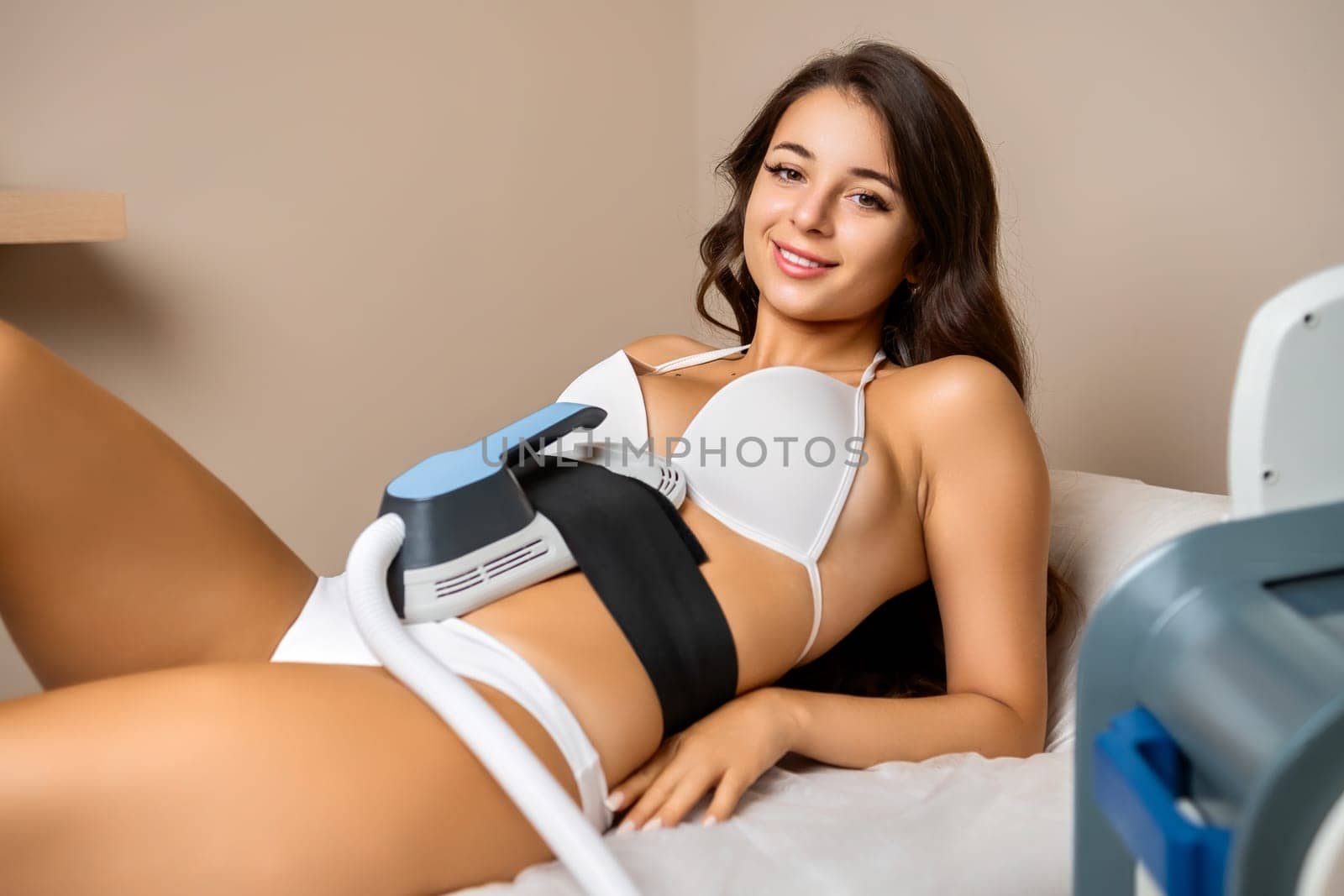 A contented young brunette lies on the couch while receiving a body sculpting treatment in spa salon