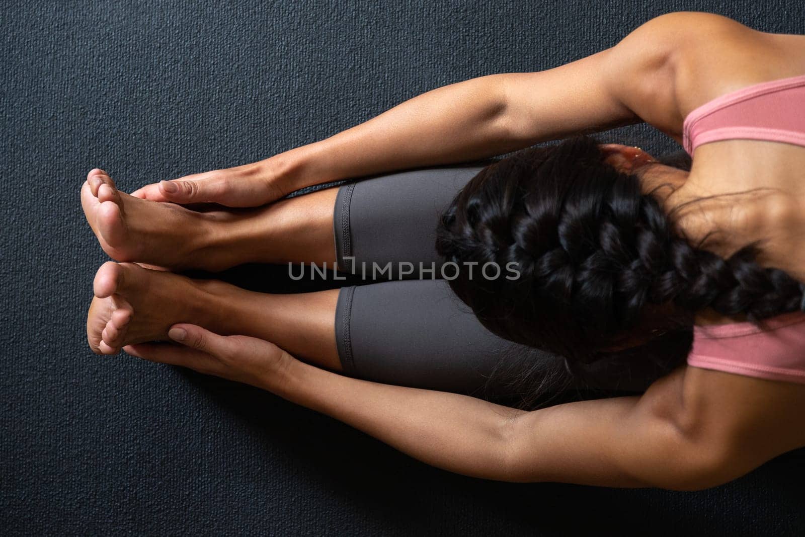 Top view close-up of woman doing yoga stretching exercise, forward bend, paschimottanasana pose on mat. by Hoverstock