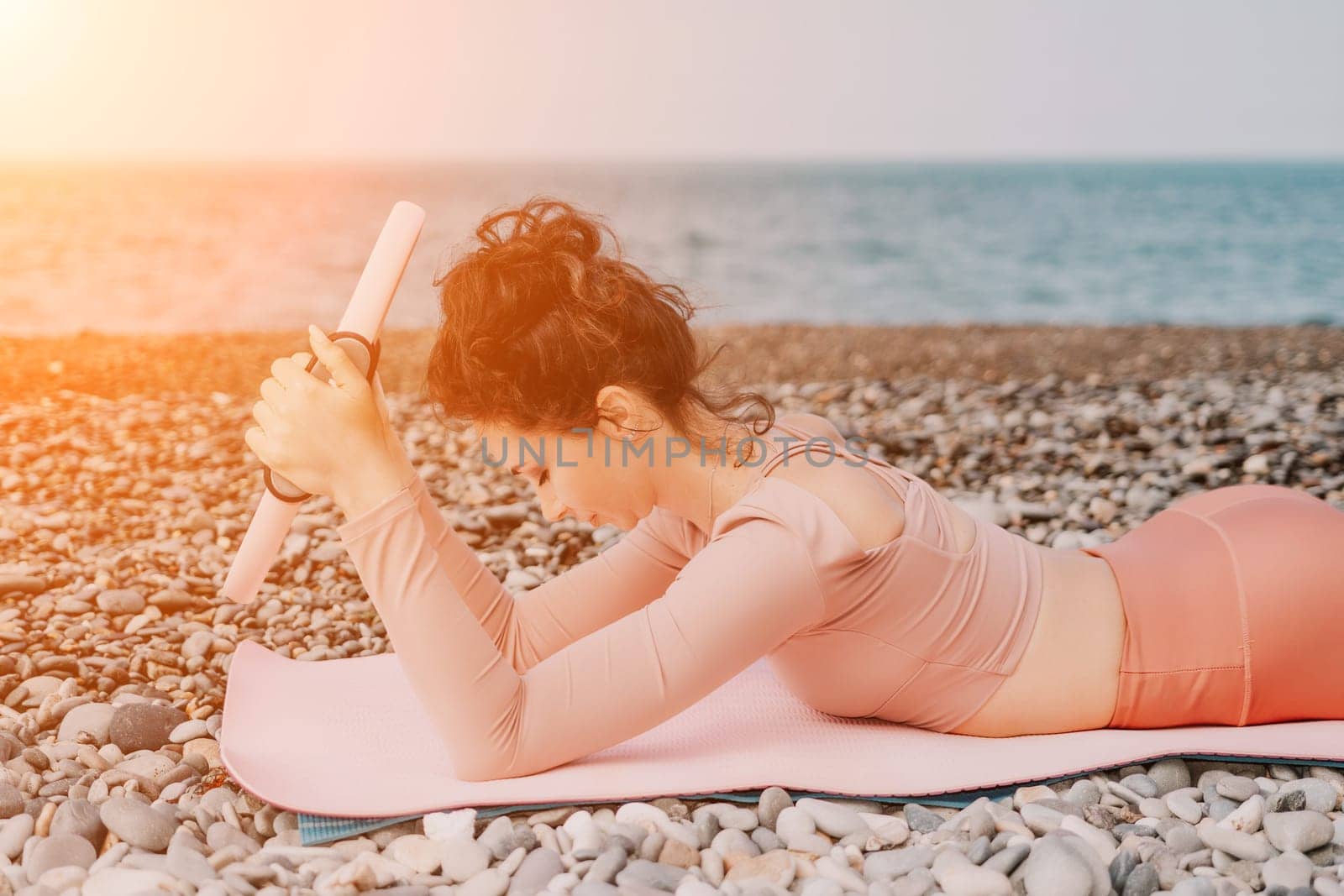 Woman sea pilates. Sporty happy middle aged woman practicing fitness on beach near sea, smiling active female training with ring on yoga mat outside, enjoying healthy lifestyle, harmony and meditation by panophotograph