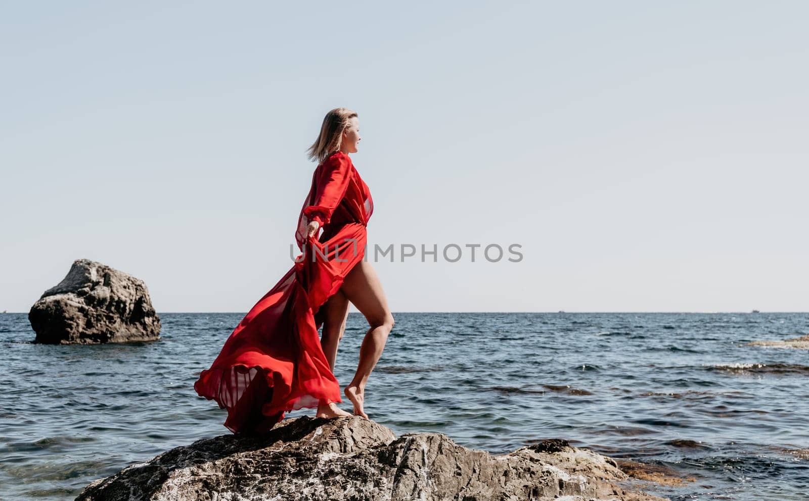 Woman travel sea. Young Happy woman in a long red dress posing on a beach near the sea on background of volcanic rocks, like in Iceland, sharing travel adventure journey