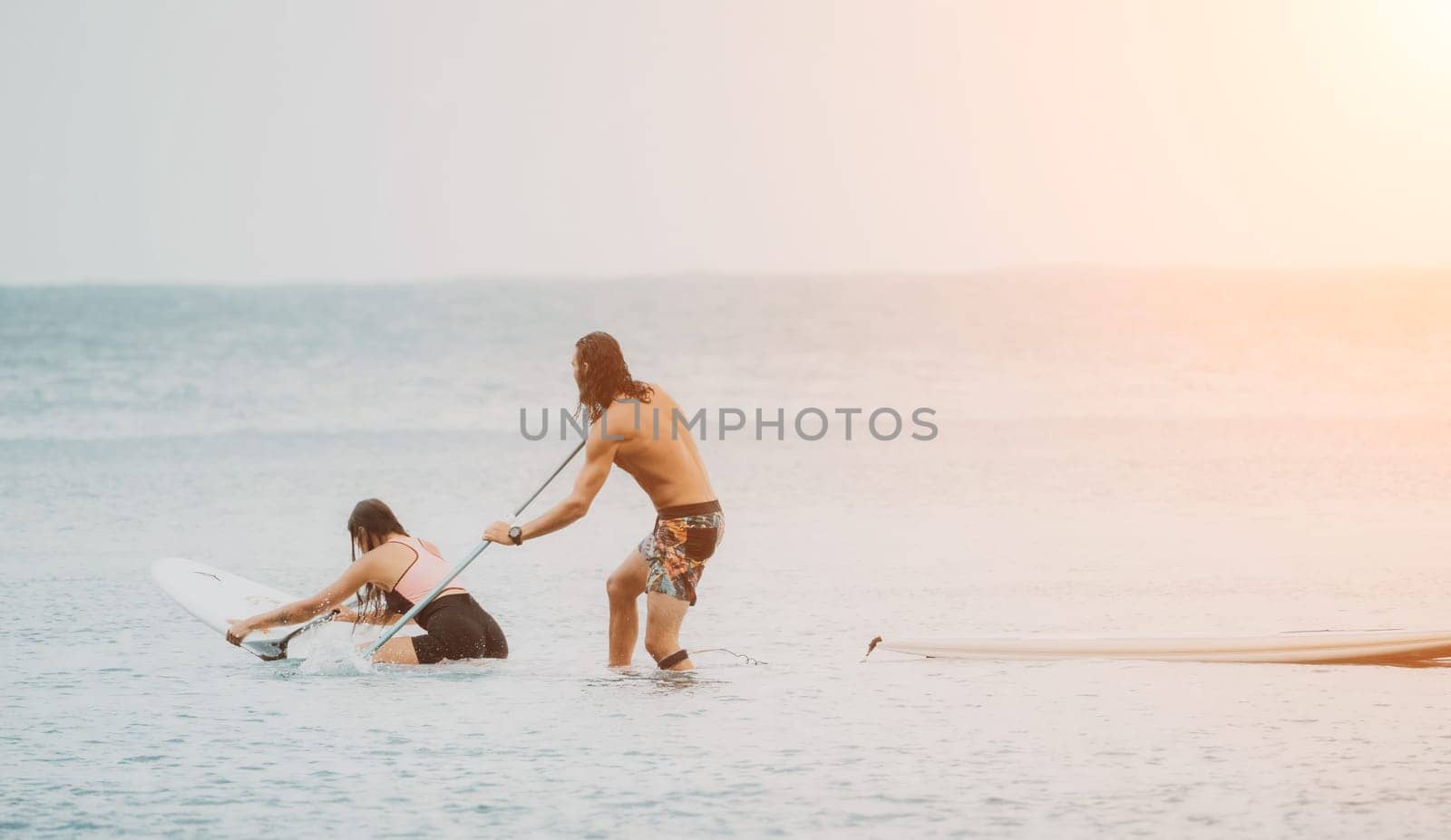 Sea woman and man on sup. Silhouette of happy young woman and man, surfing on SUP board, confident paddling through water surface. Idyllic sunset. Active lifestyle at sea or river