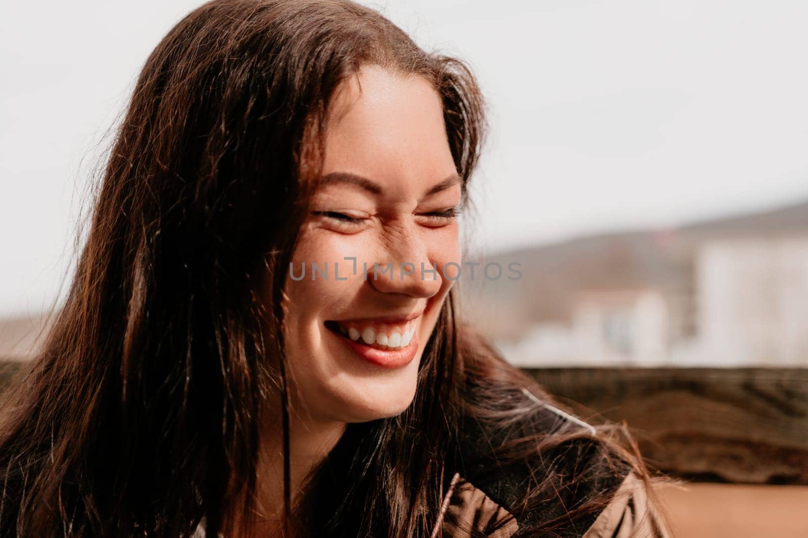 Happy young smiling woman with freckles outdoors portrait. Soft sunny colors. Outdoor close-up portrait of a young brunette woman and looking to the camera, posing against nature background.