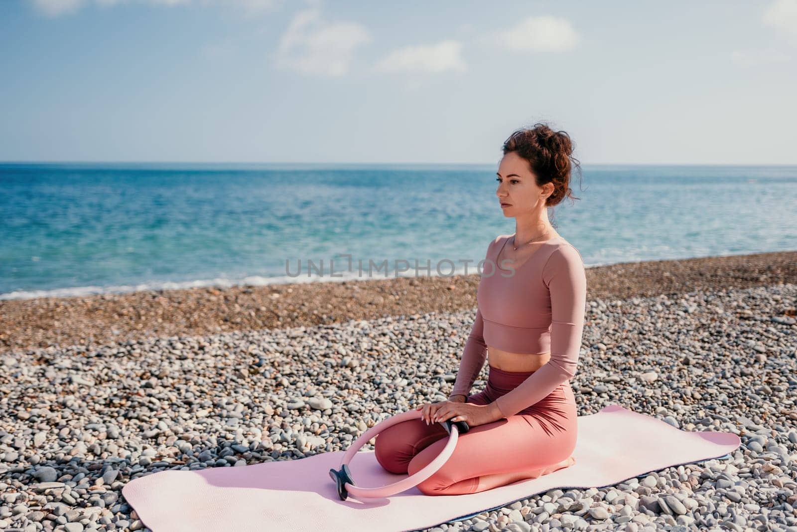 Woman sea pilates. Sporty happy middle aged woman practicing fitness on beach near sea, smiling active female training with ring on yoga mat outside, enjoying healthy lifestyle, harmony and meditation by panophotograph