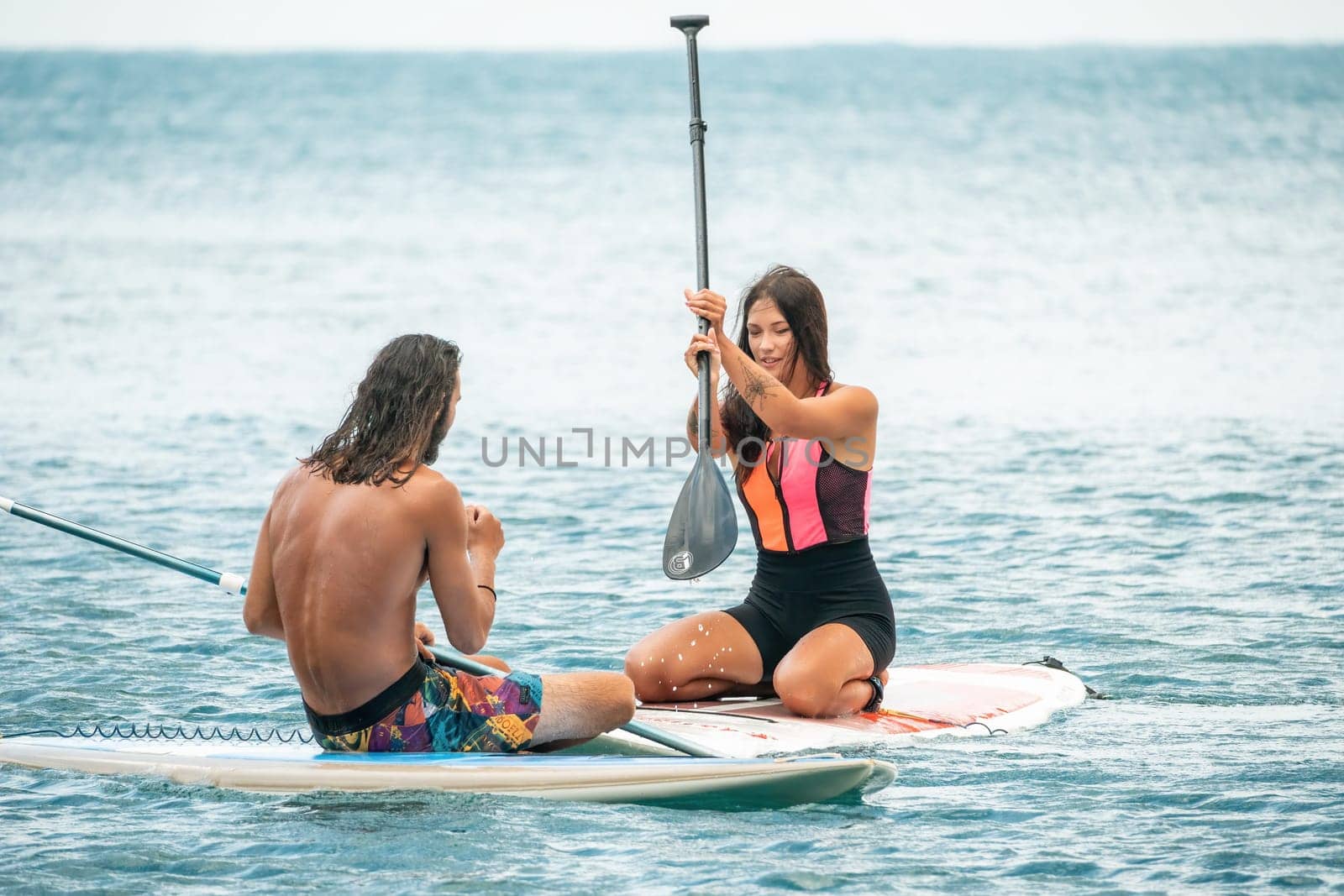 Sea woman and man on sup. Silhouette of happy young woman and man, surfing on SUP board, confident paddling through water surface. Idyllic sunset. Active lifestyle at sea or river