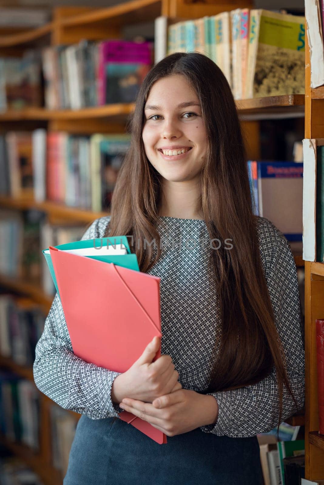Happy smiling girl with folders in library by VitaliiPetrushenko