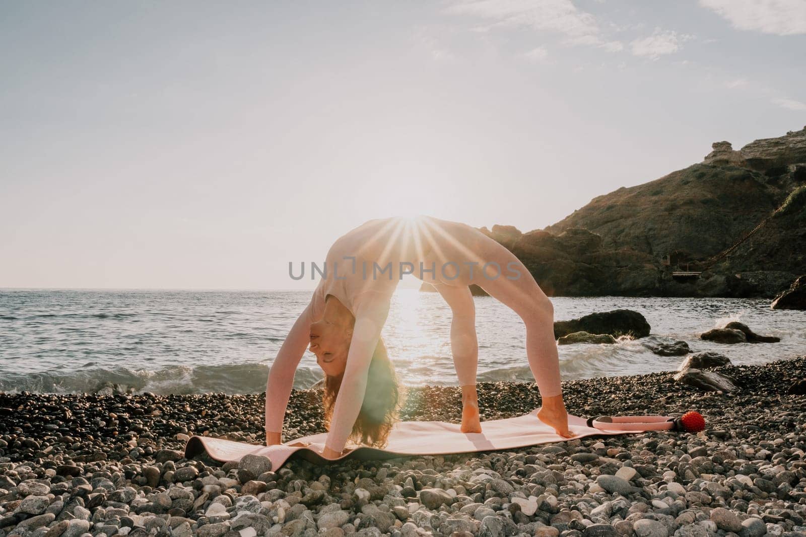 Woman sea yoga. Happy woman with black hair doing Pilates with the ring on the yoga mat near the sea on the pebble beach. Female fitness yoga concept. Healthy lifestyle, harmony and meditation. by panophotograph