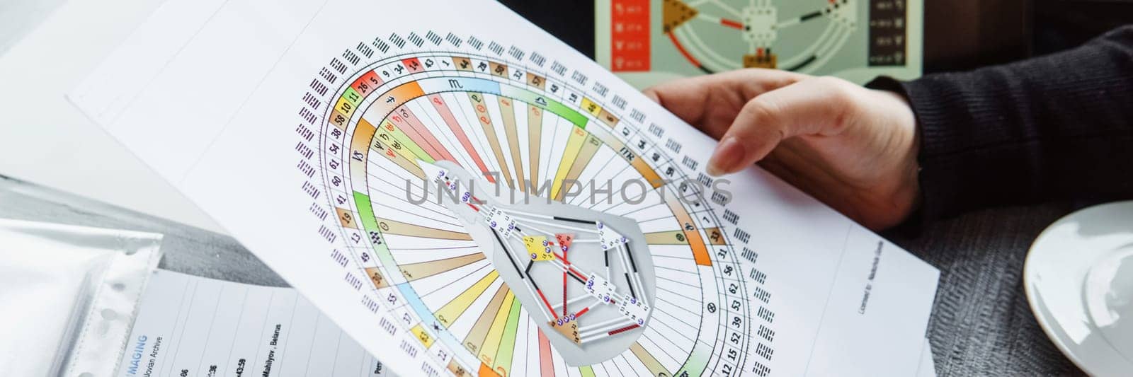 TVER, RUSSIA - FEBRUARY 12, 2023: A woman at the table is studying a rave mandala by human design. Rave mandala on the table close-up. The concept of esoteric teachings