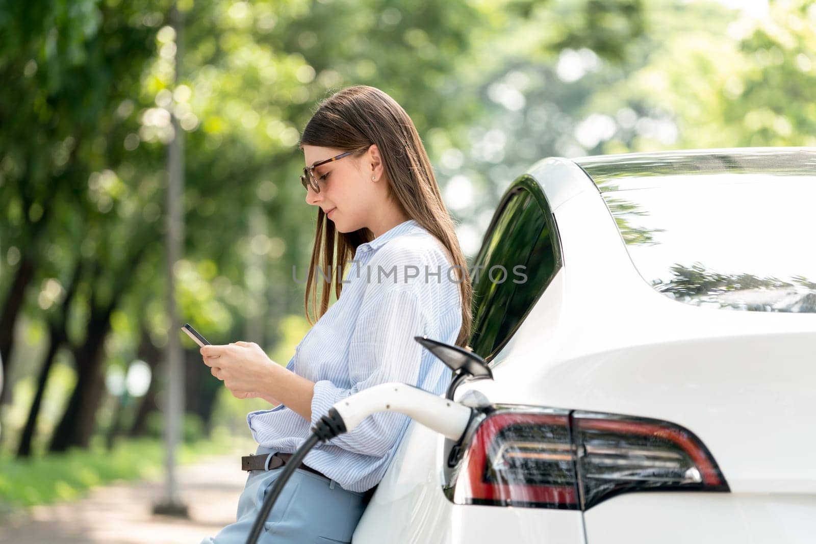 Young woman using smartphone to pay for electric car charging. Exalt by biancoblue