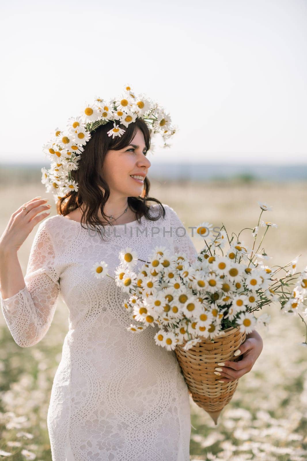Happy woman in a field of daisies with a wreath of wildflowers on her head. woman in a white dress in a field of white flowers. Charming woman with a bouquet of daisies, tender summer photo by Matiunina