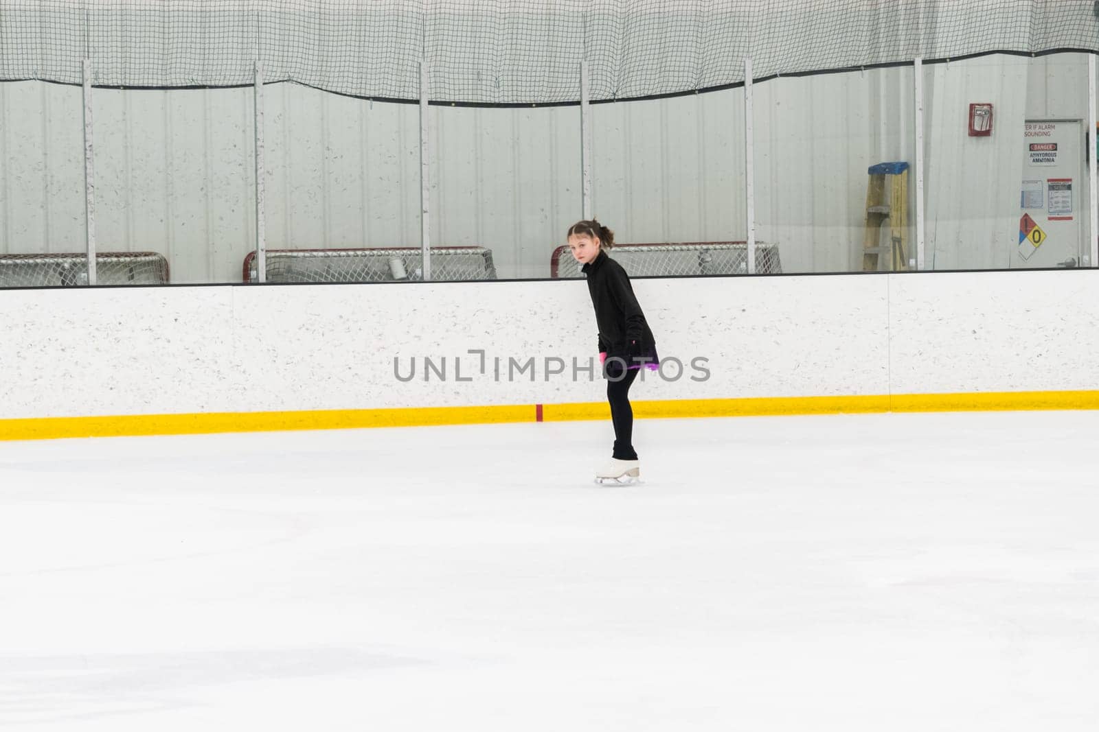 Young girl perfecting her figure skating routine while wearing her competition dress at an indoor ice rink.