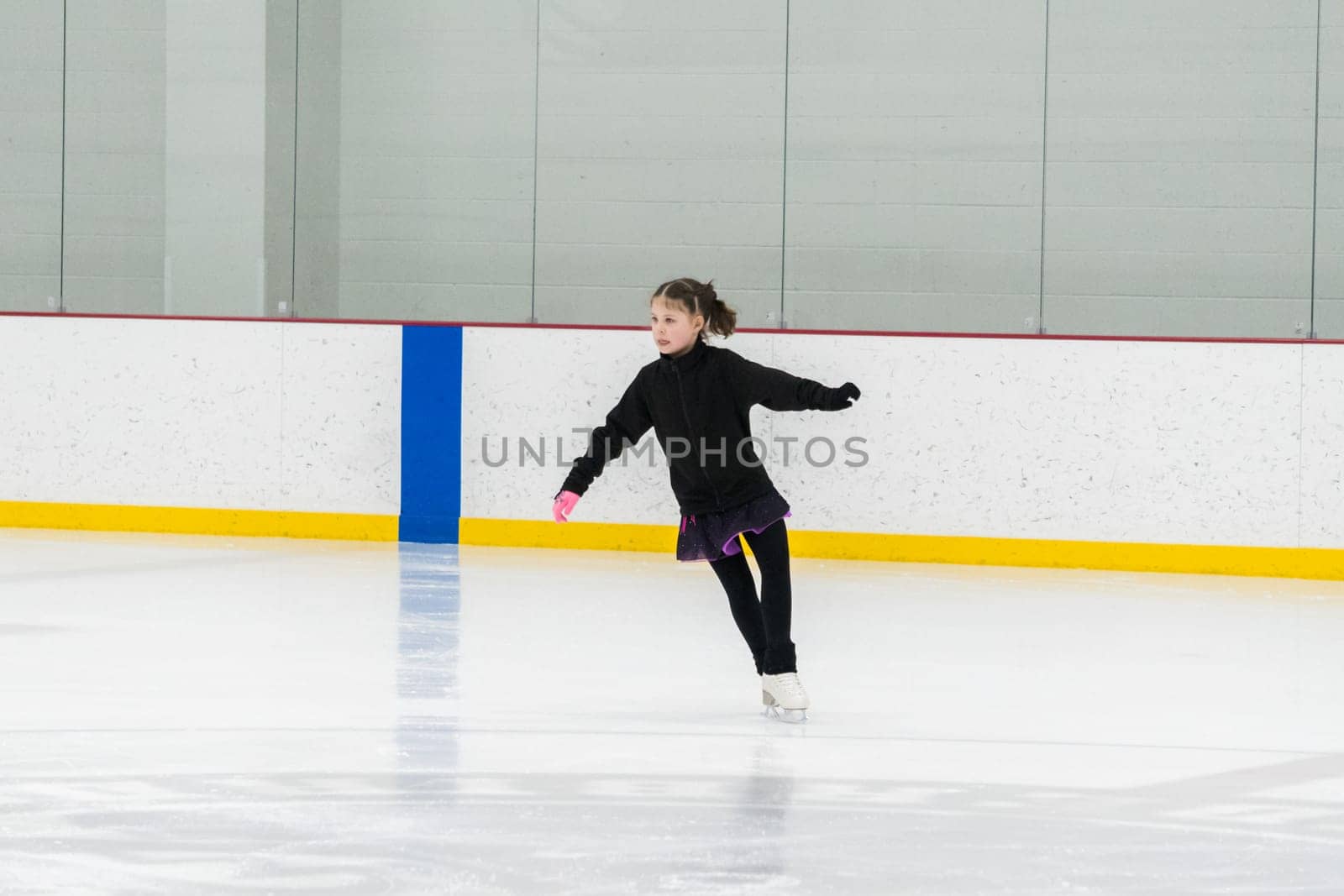 Young girl perfecting her figure skating routine while wearing her competition dress at an indoor ice rink.